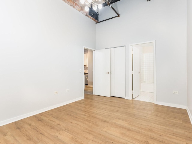 unfurnished bedroom with connected bathroom, a towering ceiling, and light hardwood / wood-style floors