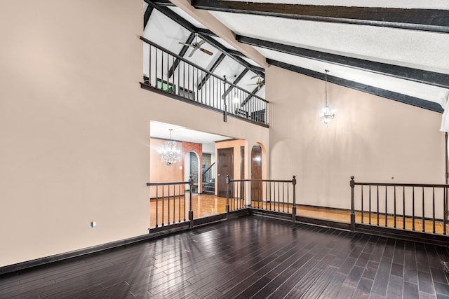 unfurnished living room featuring hardwood / wood-style flooring, ceiling fan with notable chandelier, beam ceiling, and high vaulted ceiling