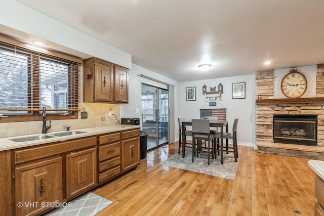 kitchen featuring decorative backsplash, light hardwood / wood-style floors, a stone fireplace, and sink