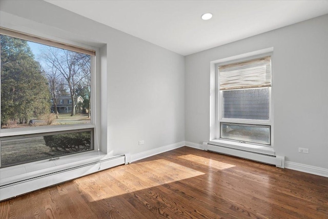 empty room featuring hardwood / wood-style flooring, a healthy amount of sunlight, and a baseboard radiator