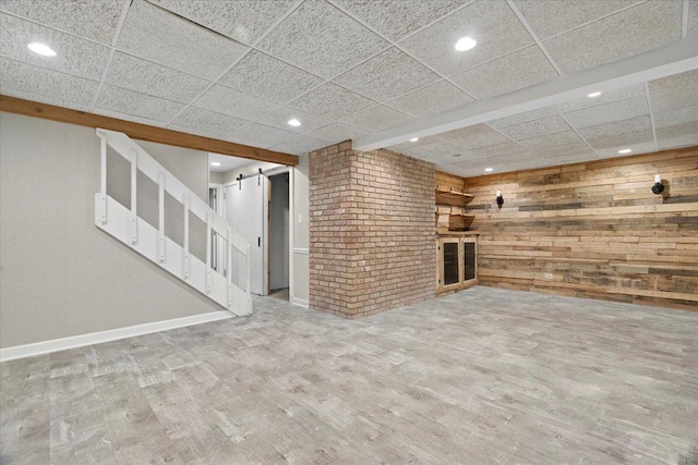 unfurnished living room with a barn door, a paneled ceiling, and hardwood / wood-style floors