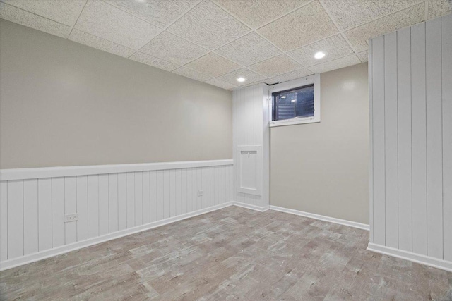 empty room featuring a paneled ceiling, light hardwood / wood-style floors, and wooden walls