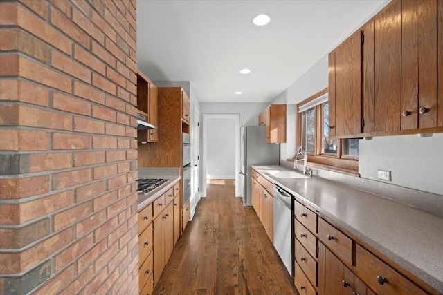 kitchen featuring brick wall, dark hardwood / wood-style floors, stainless steel appliances, and sink