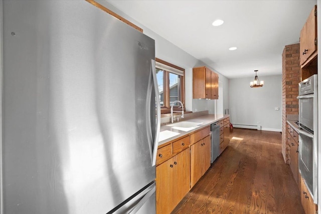 kitchen with sink, dark wood-type flooring, stainless steel appliances, a baseboard radiator, and a notable chandelier