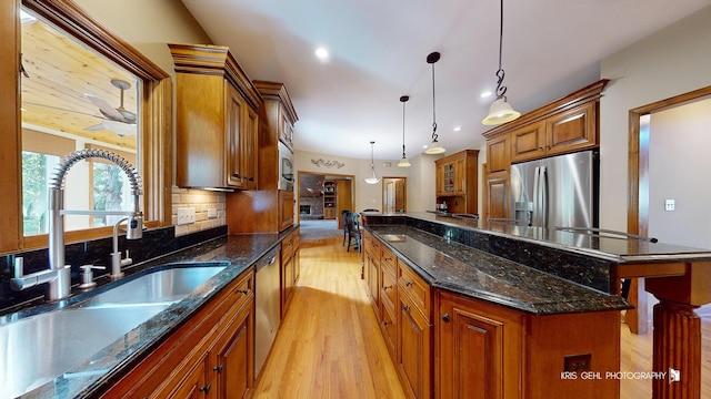 kitchen with decorative light fixtures, stainless steel appliances, a kitchen island, backsplash, and sink