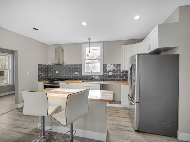 kitchen with butcher block countertops, wall chimney exhaust hood, plenty of natural light, and stainless steel appliances