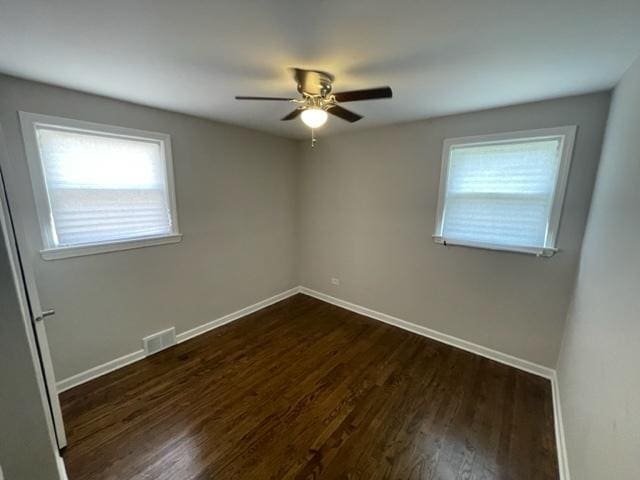 empty room featuring dark wood-style floors, a ceiling fan, visible vents, and baseboards