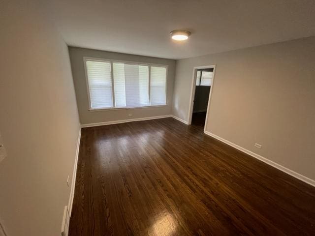 unfurnished room with baseboards and dark wood-type flooring