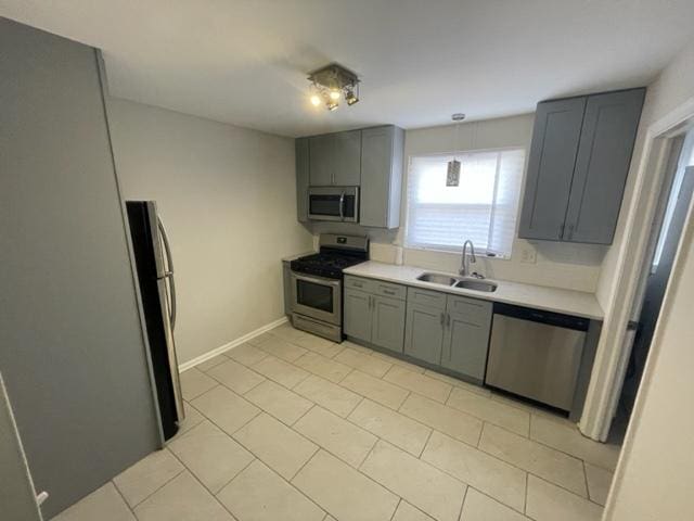 kitchen featuring light countertops, gray cabinetry, appliances with stainless steel finishes, a sink, and baseboards