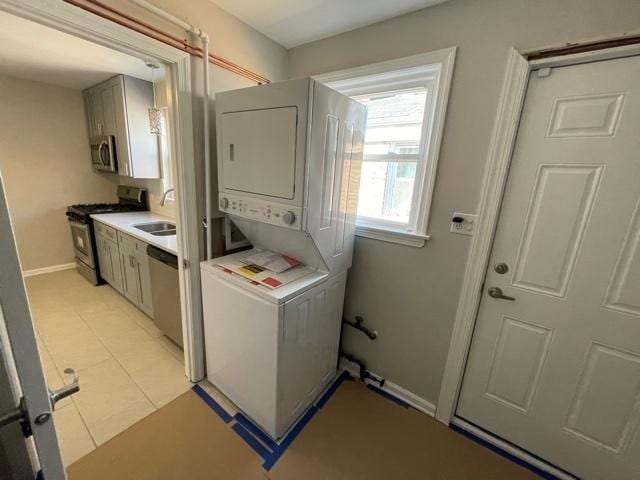 washroom featuring laundry area, light tile patterned floors, baseboards, stacked washer / drying machine, and a sink