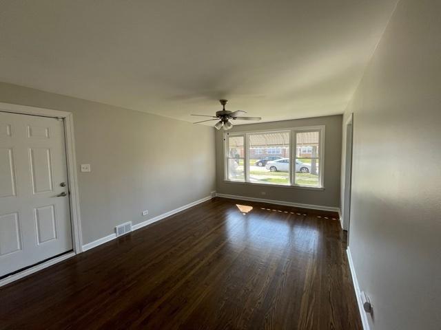 spare room featuring a ceiling fan, dark wood-style flooring, visible vents, and baseboards