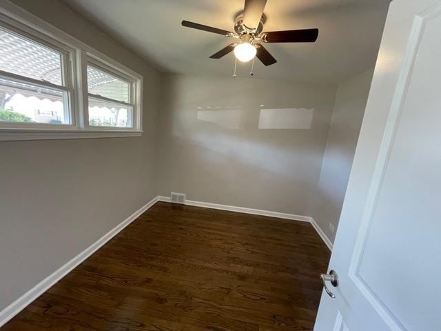 spare room with a ceiling fan, dark wood finished floors, visible vents, and baseboards