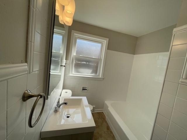 full bath featuring a wainscoted wall, tile walls, toilet, vanity, and tile patterned flooring