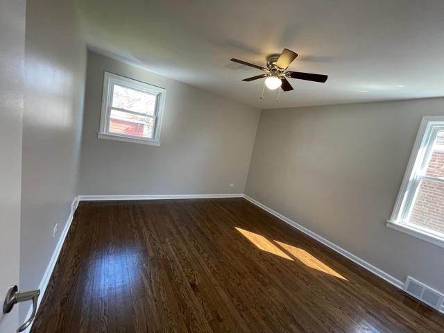 spare room featuring a ceiling fan, dark wood-style flooring, visible vents, and baseboards