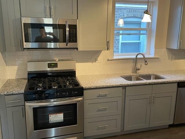 kitchen featuring light stone counters, stainless steel appliances, a sink, gray cabinets, and tasteful backsplash