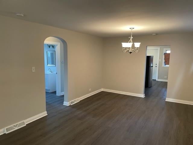 unfurnished room featuring dark wood-style floors, arched walkways, visible vents, and baseboards