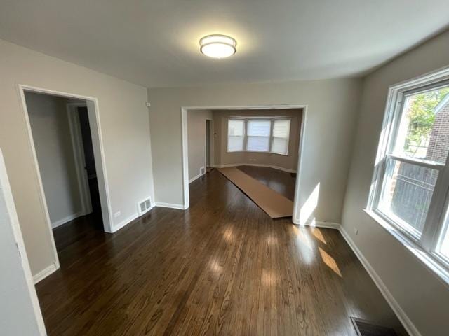 spare room with dark wood-type flooring, visible vents, and baseboards