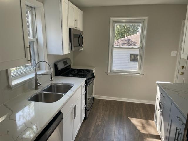 kitchen with dark wood finished floors, stainless steel appliances, white cabinetry, a sink, and light stone countertops