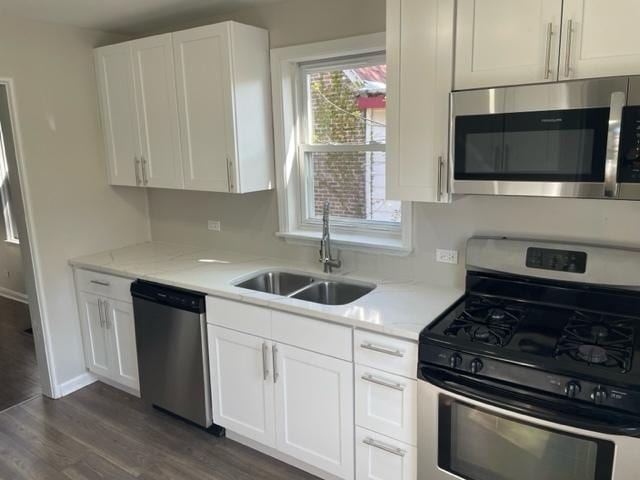 kitchen featuring dark wood-style flooring, a sink, white cabinetry, appliances with stainless steel finishes, and light stone countertops