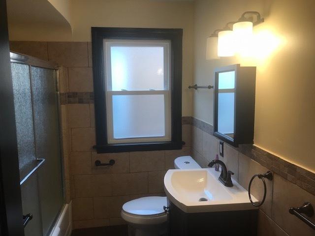 full bath with toilet, enclosed tub / shower combo, tile walls, and vanity