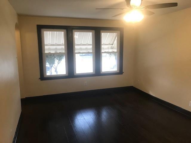 unfurnished room with dark wood-type flooring, arched walkways, baseboards, and a ceiling fan