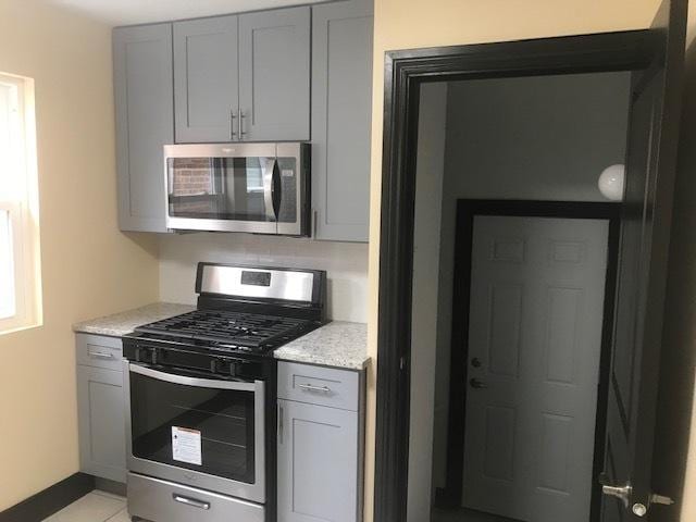 kitchen with appliances with stainless steel finishes, gray cabinets, light stone counters, and light tile patterned flooring