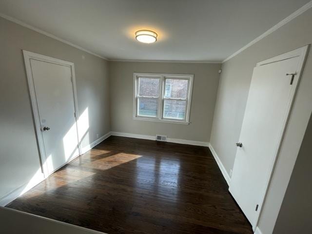 spare room featuring baseboards, visible vents, dark wood-style flooring, and ornamental molding