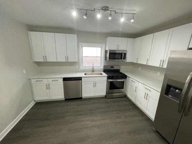 kitchen featuring dark wood-style floors, stainless steel appliances, white cabinetry, a sink, and baseboards