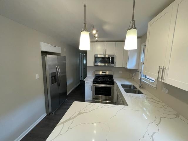 kitchen featuring appliances with stainless steel finishes, light stone counters, hanging light fixtures, white cabinetry, and a sink