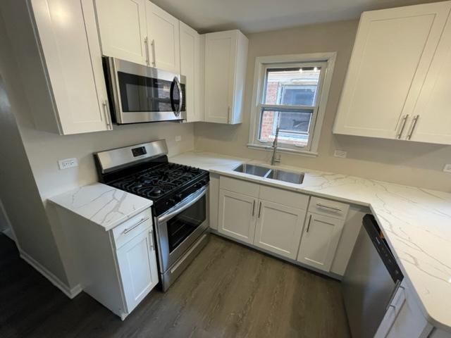 kitchen featuring appliances with stainless steel finishes, white cabinets, a sink, and light stone countertops