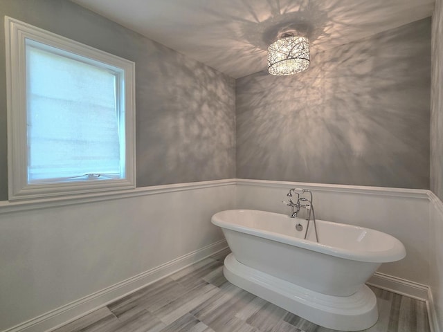 full bathroom with healthy amount of natural light, a freestanding bath, baseboards, and wood finished floors
