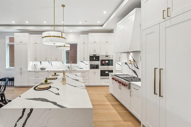 kitchen featuring white cabinetry, premium range hood, hanging light fixtures, and light hardwood / wood-style flooring