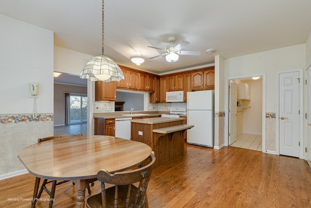 kitchen with pendant lighting, white appliances, light hardwood / wood-style floors, and a kitchen island