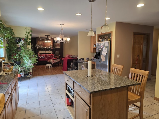 kitchen with stainless steel fridge, ceiling fan with notable chandelier, decorative light fixtures, light hardwood / wood-style flooring, and a kitchen island