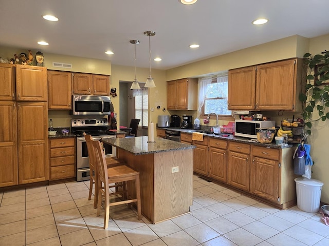 kitchen with dark stone counters, stainless steel appliances, pendant lighting, light tile patterned floors, and a kitchen island