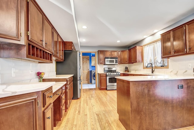 kitchen with sink, stainless steel appliances, light wood-type flooring, and washer / dryer