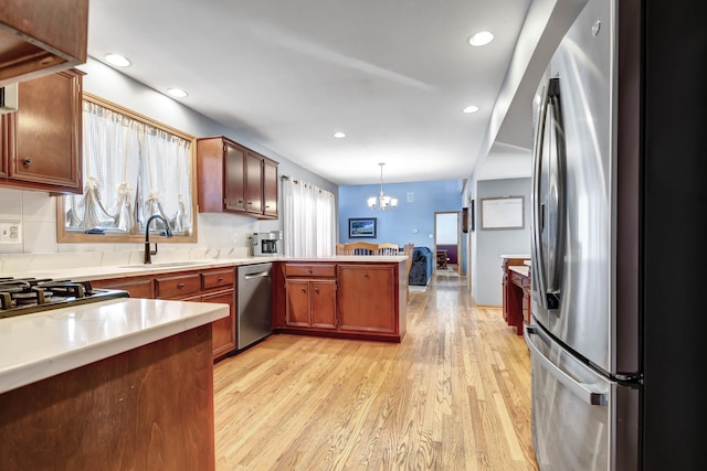 kitchen featuring stainless steel appliances, sink, decorative light fixtures, light hardwood / wood-style floors, and kitchen peninsula