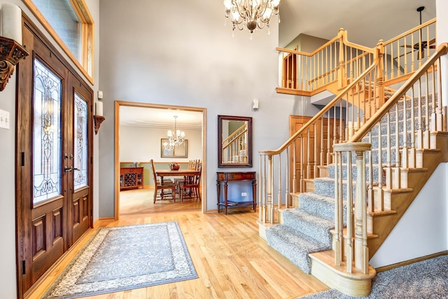 foyer entrance featuring a towering ceiling, french doors, hardwood / wood-style floors, ornamental molding, and a notable chandelier