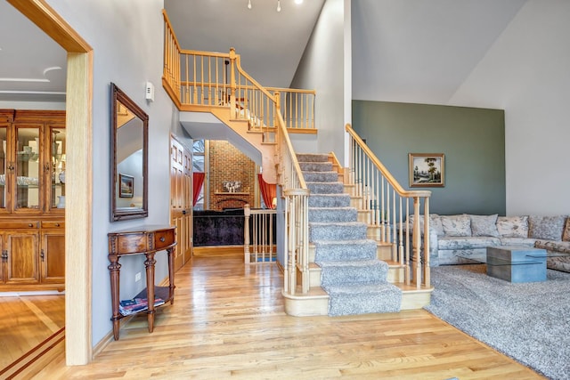 staircase with a brick fireplace, hardwood / wood-style floors, and a towering ceiling