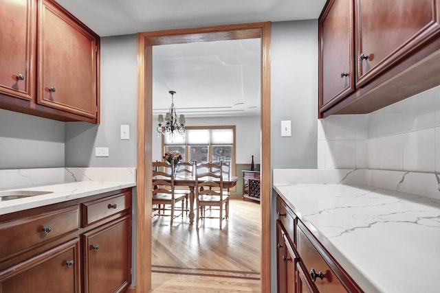 kitchen with an inviting chandelier, backsplash, light stone counters, and light hardwood / wood-style flooring