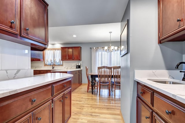 kitchen with sink, pendant lighting, light stone counters, and light hardwood / wood-style flooring