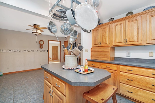 kitchen with a kitchen bar, dark tile patterned flooring, a kitchen island, and ceiling fan