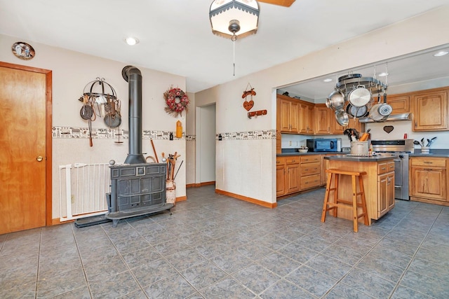 kitchen featuring a wood stove, a center island, stainless steel appliances, a breakfast bar, and dark tile patterned flooring