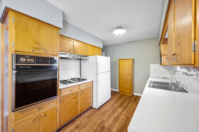 kitchen featuring white refrigerator, decorative backsplash, light wood-type flooring, black oven, and stainless steel gas cooktop