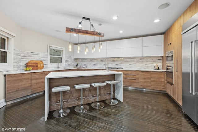 kitchen with sink, white cabinetry, hanging light fixtures, a kitchen island with sink, and decorative backsplash