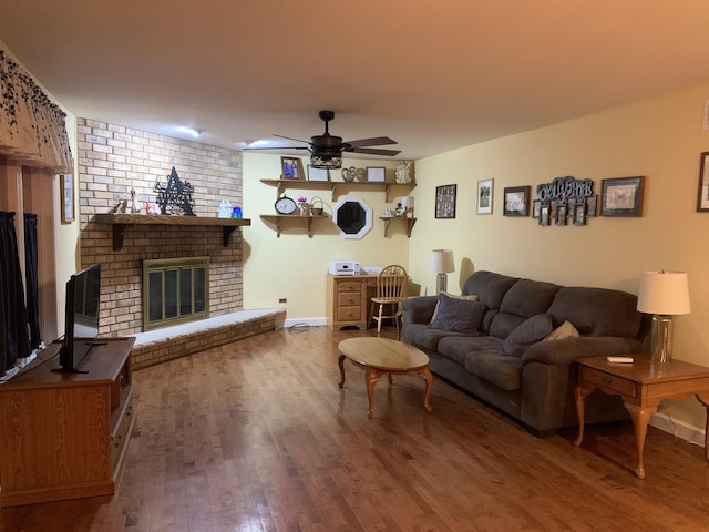 living room with a brick fireplace, wood-type flooring, and ceiling fan