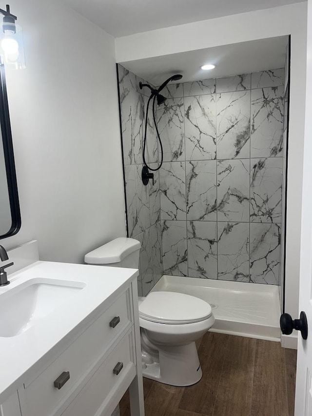 bathroom featuring vanity, toilet, a tile shower, and wood-type flooring