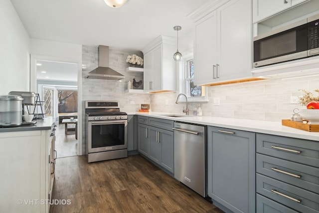 kitchen featuring pendant lighting, appliances with stainless steel finishes, sink, gray cabinetry, and wall chimney range hood