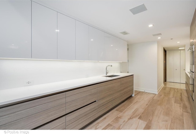 kitchen featuring light wood finished floors, visible vents, white cabinetry, a sink, and modern cabinets