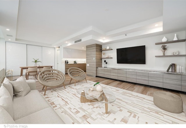 living room featuring light wood-type flooring, a raised ceiling, visible vents, and recessed lighting